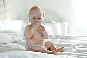 Cute little baby in diaper with pacifier sitting on bed