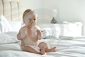 Cute little baby in diaper with pacifier sitting on bed at home. Space for text