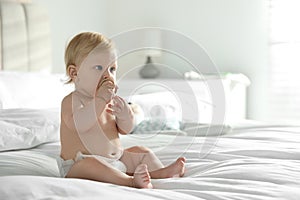 Cute little baby in diaper with pacifier sitting on bed. Space for text