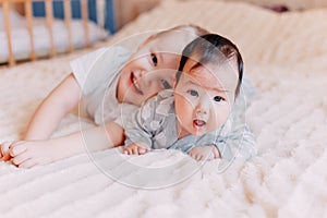 Cute little baby with elder brother lying on bed at home