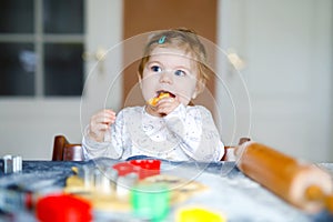 Cute little baby girl baking gingerbread Christmas cookies at home. Adorable blond happy healthy child having fun in