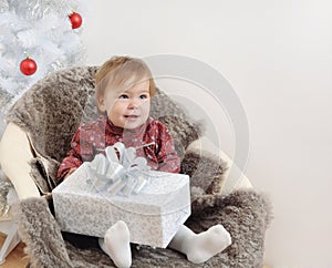 Cute little baby girl with big gift in hands near Christmas tree
