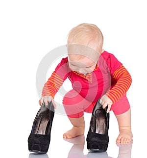 Cute little baby girl trying on her mother's shoes on white back