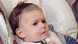 Cute little baby girl eating baby food with hands on high chair in home kitchen. Close-up