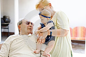 Cute little baby girl with grandmother and grandfather on summer day in garden