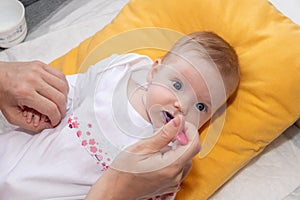 Cute little baby girl lying on the bed and eating rice soup with spoon. Mother feeding her baby girl. The baby girl is four months