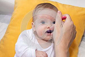 Cute little baby girl lying on the bed and eating rice soup with spoon. Mother feeding her baby girl. The baby girl is four months