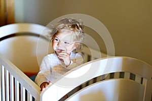 Cute little baby girl lying in cot after sleeping. Healthy happy child in bed climbing out.