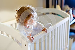 Cute little baby girl lying in cot after sleeping. Healthy happy child in bed climbing out.