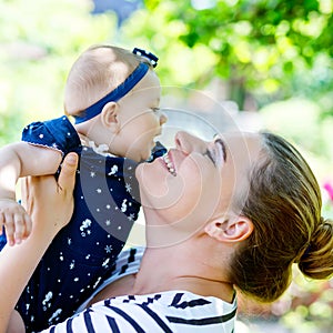 Cute little baby girl with mother on summer day in garden. Happy woman holding smiling child on arm. Kissing, hugging..