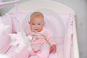 Cute little baby girl in a pink cot.