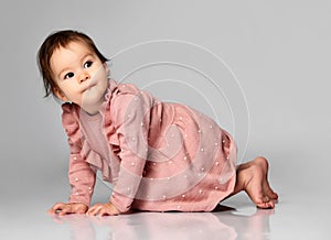 Cute little baby girl in a pink dress crawls on a gray background in the studio.