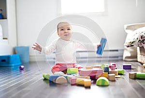 Cute little baby girl play with plastic bricks sitting indoors on a tiles floor