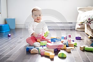 Cute little baby girl play with plastic bricks sitting indoors on a tiles floor