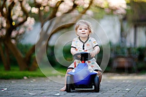 Cute little baby girl playing with blue small toy car in garden of home or nursery. Adorable beautiful toddler child