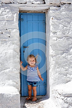 A cute, little baby girl stands on a traditional blue door, Mykonos island, Greece