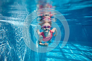 Cute little baby girl, toddler in pink swimsuit diving, swimming underwater in swimming pool. Water sports activity