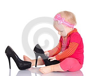 Cute little baby girl trying on her mother's shoes on white back