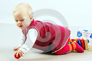 Cute little baby girl wearing a red clothes is sitting on the floor and playing colorful wooden toys, horizontal view.