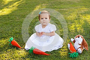 Cute little baby girl in white dress with toy rabbit and carrot