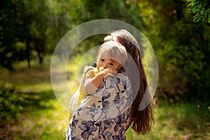 Cute little baby girl in yellos dress hugs her mother at the green garden