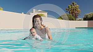 Cute little baby and his mother having swimming lesson in the pool. The mother is holding baby in his hands and