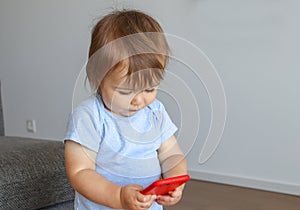Cute little baby holds mobile phone in his hands and looking attentively at screen.