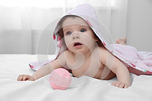 Cute little baby in hooded towel after bathing playing with toy on bed at home