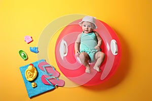 Cute little baby with inflatable ring and beach accessories on yellow background, top view