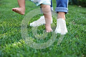 Cute little baby learning to walk with his nanny on green grass outdoors