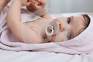 Cute little baby with pacifier in hooded towel after bathing on bed, closeup