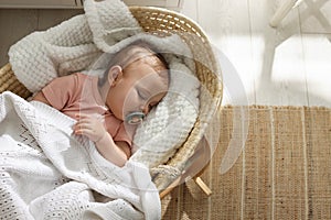 Cute little baby with pacifier sleeping in wicker crib at home, top view. Space for text