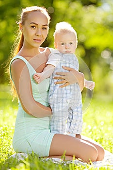 Cute little baby in the park with mother on the grass. Sweet baby and mom outdoors. Smiling emotional kid with mum on a walk. Sm