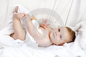 Cute little baby playing with own feet after taking bath. Adorable beautiful girl wrapped in white towels
