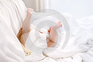 Cute little baby playing with own feet after taking bath. Adorable beautiful girl wrapped in white towels