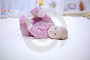 Cute little baby plays with his legs on the bed in bedroom