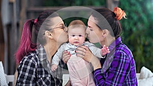 Cute little baby posing looking at camera during two happy mother kissing and hugging him