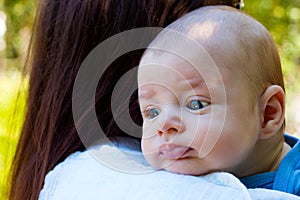 Portrait of beautiful baby in loving mother`s arms, newborn head is resting on the shoulder to burp, cute infant face close up