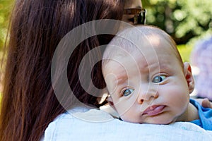 Portrait of beautiful baby with blue eyes and cute face, mother with brown hair caring infant on shoulder, baby burping position