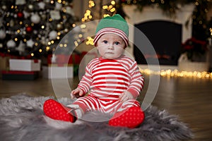 Cute little baby in Santa`s elf clothes on floor at home. Christmas celebration