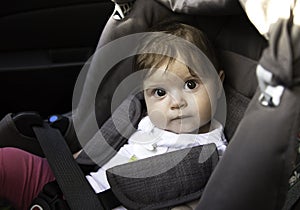 Cute little baby sits fastened in a car seat ready for a ride. Child safety concept