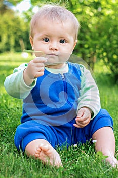 Cute little baby sitting on the grass in park and playing with a blade of grass