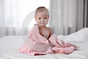 Cute little baby with soft pink towel on bed after bath