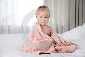 Cute little baby with soft pink towel on bed after bath