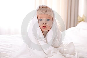 Cute little baby with soft towel on bed after bath