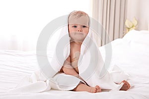 Cute little baby with soft towel on bed after bath