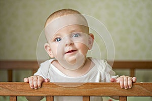 Cute little baby standing in a bed. Smiling child playing in bed. Kid portrait at nursery. Happy childhood concept