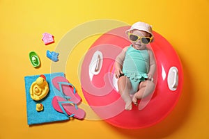 Cute little baby in sunglasses with inflatable ring and beach accessories on yellow background, top view