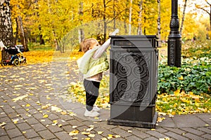 cute little baby throws trash into trash can in autumn park. instilling cultural norms from birth