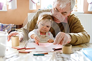 Cute little baby toddler girl and handsome senior grandfather painting with colorful pencils at home. Grandchild and man